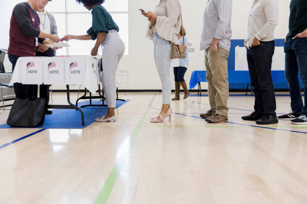 istock Mature male volunteers help unrecognizable people lined up to vote 1204436334