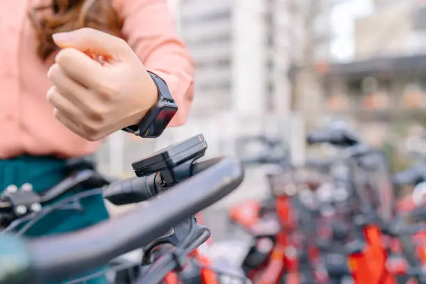 Photo of Young businesswoman using smart watch to rent sharing bicycle