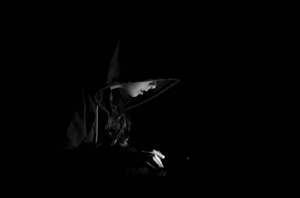 istock Girl hacker with hood in darkness working on laptop computer 1204444516