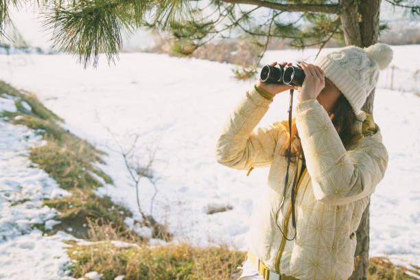 istock The girl in a White cap with a backpack in the winter in a forest looking through binoculars 1204444545