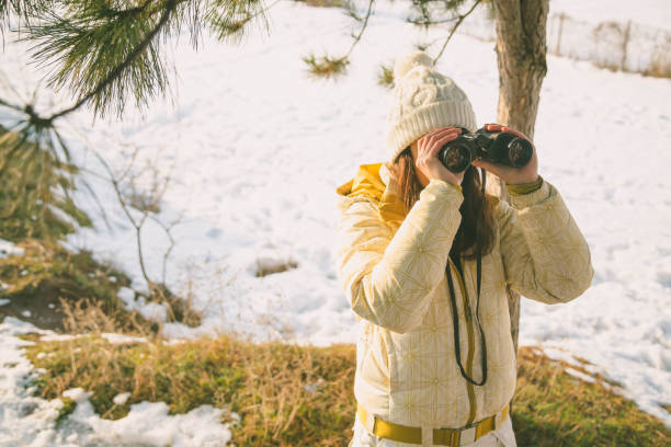 istock The girl in a White cap with a backpack in the winter in a forest looking through binoculars 1204444557