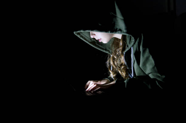 Girl hacker with hood in darkness working on laptop computer