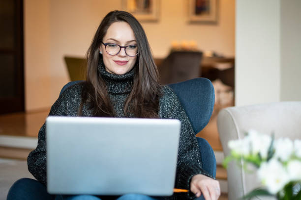 istock Shot of young woman using notebook while sitting on armchair at home 1204453596