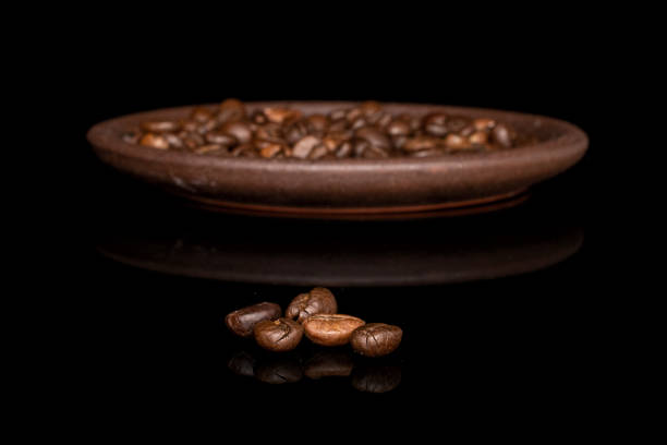 Lot of whole fresh coffee bean front focus with brown ceramic coaster isolated on black glass