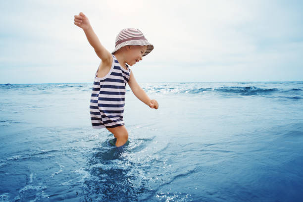three years old boy playing at the beach in the water. Happy child on family vacations at sea in summer. Summertime tourism and travel concept