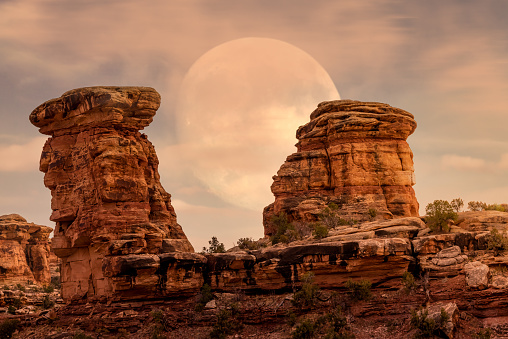 Hoodoos geological formation portrat in Canyonlands national Park with hazy full moon sky rising behind it