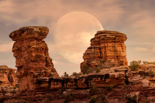 Hoodoos geological formation portrat in Canyonlands national Park with hazy full moon sky rising behind it stock photo