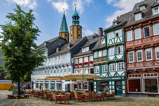 Cafes with tables and parasols outside in the cobbled Schuhhof market square of Goslar Lower Saxony, Germany with the twin spires of the Market Church of St Cosmas and Damian in the background.