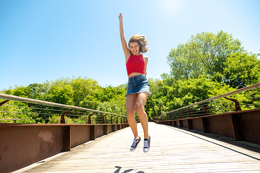 Happy young beautiful woman in red top and mini skirt jumping on a bridge in a sunny day