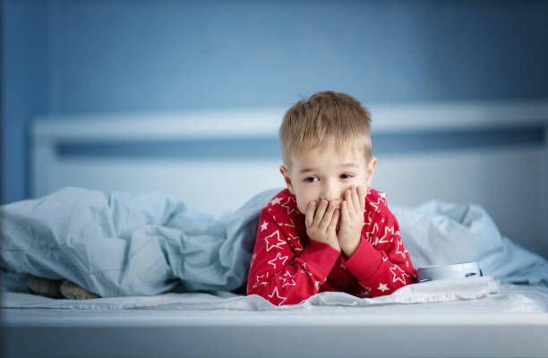 Sleepy boy lying in bed with blue beddings Sleepy boy lying in bed with blue beddings. Tired child in bedroom. Little kid lying awake in red pajamas with toothacheSleepy boy lying in bed with blue beddings. Tired child in bedroom sleeping. Little kid lying asleep in red pajamas with alarm clock only boys stock pictures, royalty-free photos & images