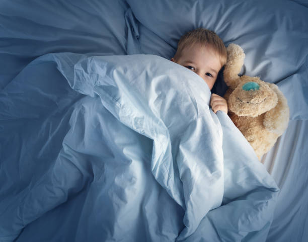 istock Sleepy boy lying in bed with white beddings 1204462155