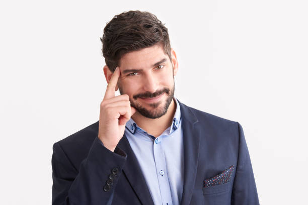 Confident young businessman studio portrait Studio portrait of young businessman with hand on his forehead looking at camera and smiling while standing at isolated white background. head in hands stock pictures, royalty-free photos & images