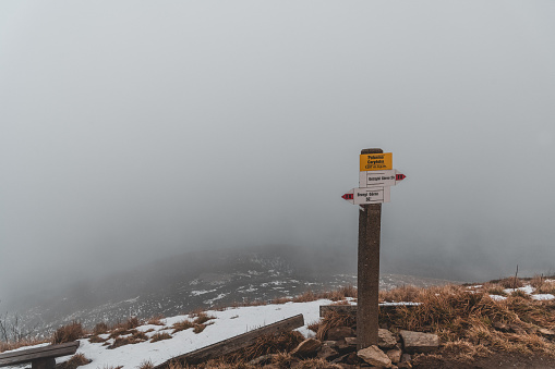 A sign showing directions and distances on the trail in the Bieszczady Mountains. Heavy clouds hang low.
