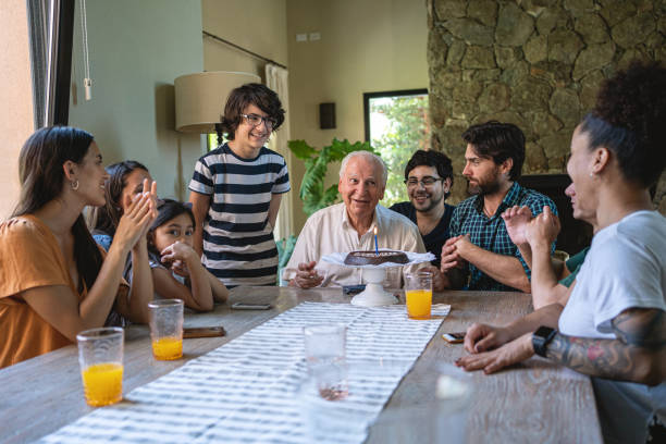 Cheerful Hispanic family surprising grandfather with birthday cake for his birthday Happy big Latin family celebrating granfather birthday together in his home with birthday cake happy birthday cousin stock pictures, royalty-free photos & images