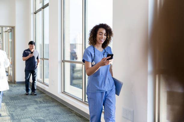 istock Female nurse walks down busy hallway while texting on phone 1204472642