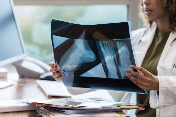 seduta alla sua scrivania, una radiologa donna fiduciosa legge le radiografie - professional occupation human foot clothing concentration foto e immagini stock