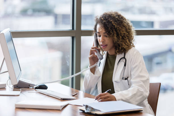 średnio dorosła kobieta lekarz wykonuje telefon w sprawie dokumentacji pacjenta - patient doctor african descent hospital zdjęcia i obrazy z banku zdjęć