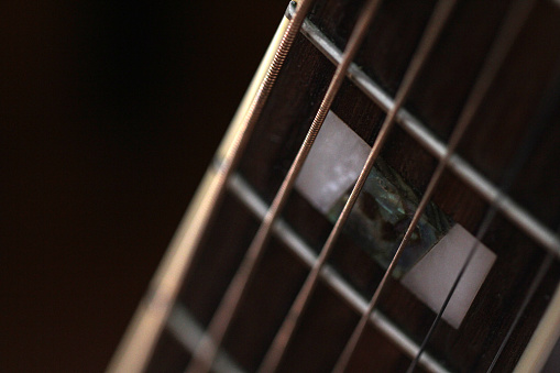 Close-up of an old acoustic guitar fretboard with rusty strings and mother of pearl inlays