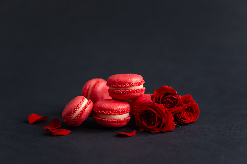 Tasty french macarons with red roses on a black background. Concept for Valentine's day. Place for text.