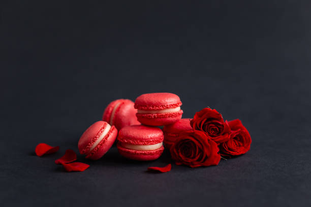 Tasty french macarons with red roses on a black background. Concept for Valentine's day. Tasty french macarons with red roses on a black background. Concept for Valentine's day. Place for text. bud candy stock pictures, royalty-free photos & images