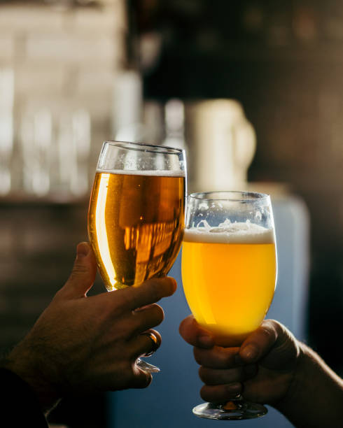 two people clink glasses with beer at the bar stock photo