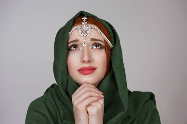 叫び。祈る女性。美しい女王美しい女性の女の子オリエンタルティッカジュエリーグリーンイスラム教徒のスカーフは、明るい未来と平和孤立した灰色の壁の背景を望んで神に向かって見上� - green tika ストックフォトと画像