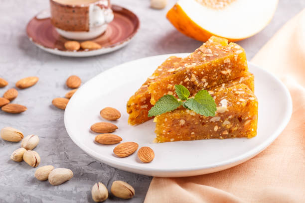 istock Traditional turkish candy cezerye made from caramelised melon, roasted walnuts, hazelnuts, cashew, pistachios on white ceramic plate and a cup of coffee on a gray concrete background. side view, close up, selective focus. 1204481486
