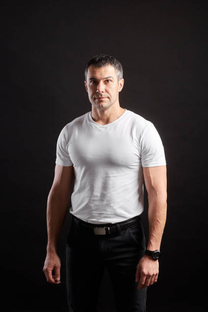 istock Handsome Athletic man in white blank t-shirt standing on black wall background 1204483899