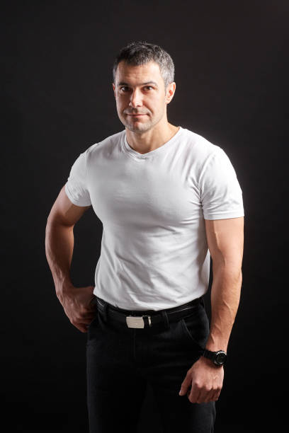 istock Handsome Athletic man in white blank t-shirt standing on black wall background 1204483920