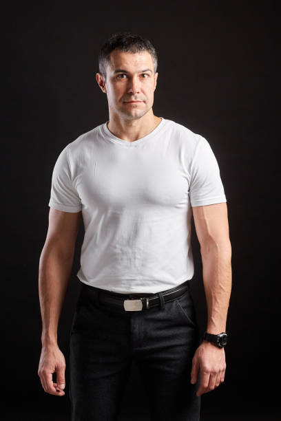 istock Handsome Athletic man in white blank t-shirt standing on black wall background 1204483999