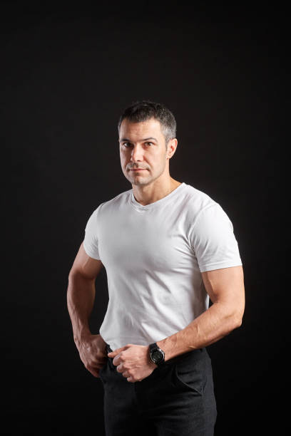 istock Handsome Athletic man in white blank t-shirt standing on black wall background 1204484106