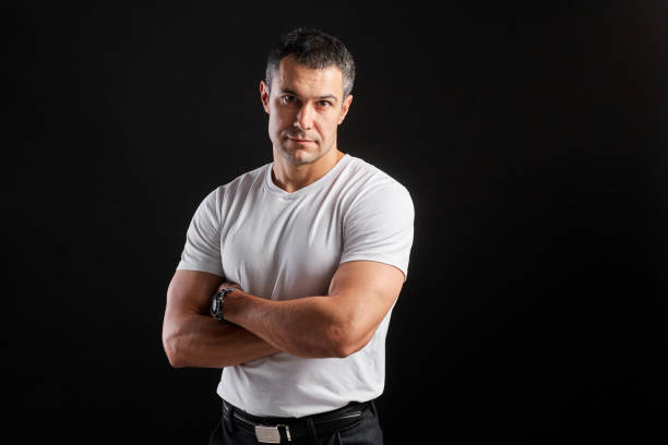 istock Handsome Athletic man in white blank t-shirt standing on black wall background 1204484750