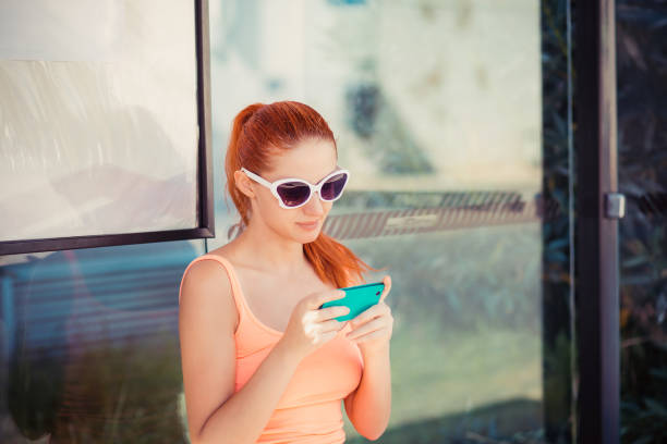 Girl texting on smartphone. Young woman using her cell phone on bus station checking message sms e-mail or bus tram schedule. Outdoors