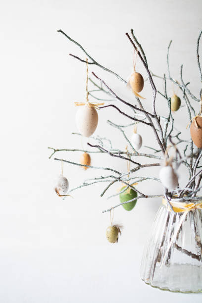 Still life with tree branches decorated with Easter eggs and feathers in glass vase stock photo