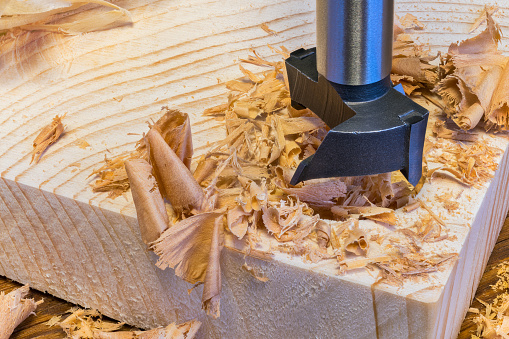 Sharp cutting tool detail. Drilling of round bore in wood by precise milling cutter. Beautiful pile of scattered curled shavings. Furniture production in joinery or cabinetry