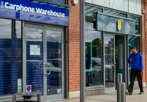 Man studies phone whilst passing phone shops Llanddudno, UK: May 06, 2019: A man checks his mobile phone whilst walking past an open EE mobile phone store. Next door is a branch of The Carphone Warehouse which has closed permanently. british telecom photos stock pictures, royalty-free photos & images