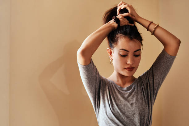 Take self improvement with the seriousness it deserves Shot of a young woman tying up her hair in preparation for a yoga session woman tying hair in ponytail getting ready for exercising stock pictures, royalty-free photos & images