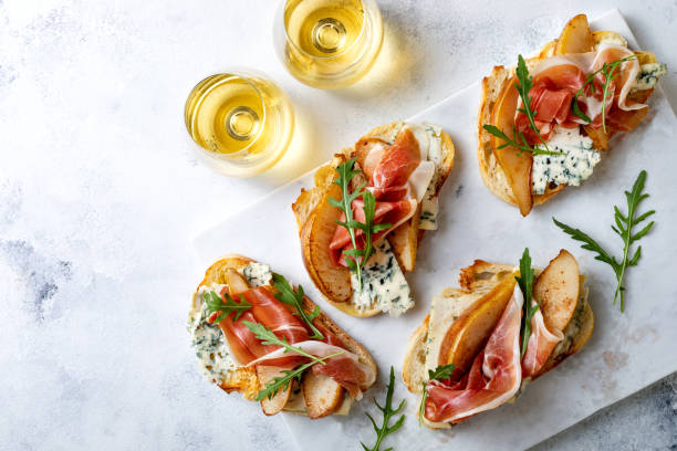 vorspeise crostini, tapas, offene sandwiches mit birne, schinken, rucola und blaukäse auf weißem marmorbrett. köstlicher snack, vorspeisen - crostini stock-fotos und bilder