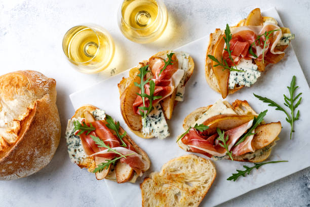 istock Appetizer crostini, tapas, open faced sandwiches with pear, prosciutto, arugula and blue cheese on white marble board. Delicious snack, appetizers 1204496039
