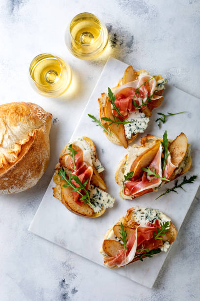 istock Appetizer crostini, tapas, open faced sandwiches with pear, prosciutto, arugula and blue cheese on white marble board. Delicious snack, appetizers 1204496040