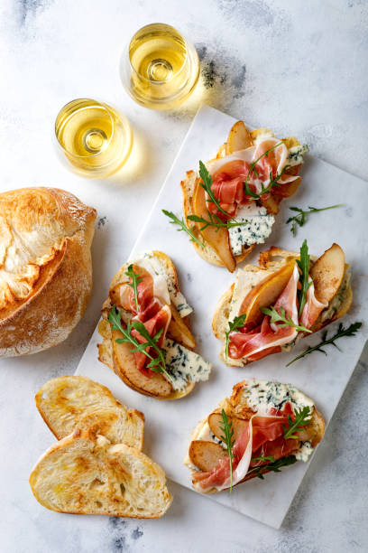 istock Appetizer crostini, tapas, open faced sandwiches with pear, prosciutto, arugula and blue cheese on white marble board. Delicious snack, appetizers 1204496070
