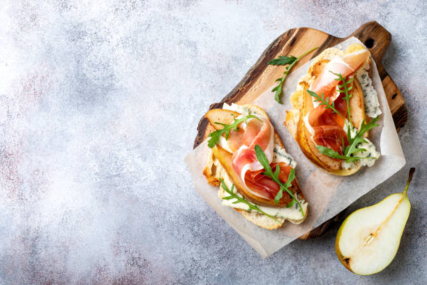 istock Appetizer crostini, tapas, open faced sandwiches with pear, prosciutto, arugula and blue cheese. Delicious snack, appetizers 1204496105