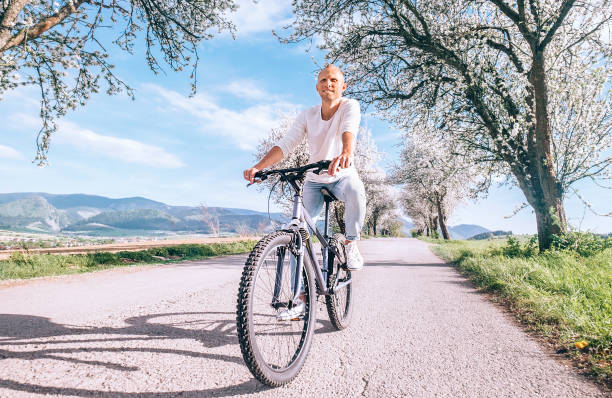 istock Happy smiling man riding a bicycle on the country road under blossom trees. Spring is comming concept image. 1204499348