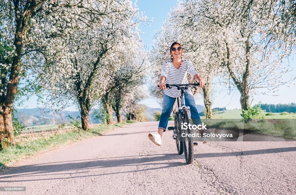 Happy smiling woman rides a bicycle on the country road under the apple blossom trees Springtime Stock Photo
