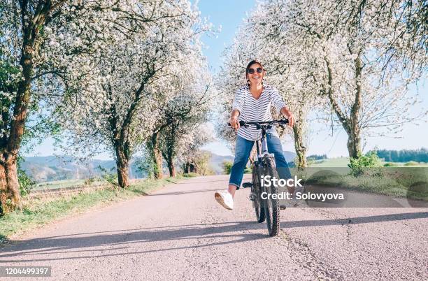 Happy Smiling Woman Rides A Bicycle On The Country Road Under The Apple Blossom Trees Stock Photo - Download Image Now