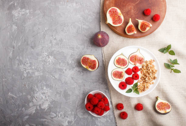 istock Yoghurt with raspberry, granola and figs in white plate on a gray concrete background and linen textile. top view, flat lay, copy space. 1204502533