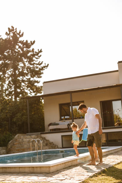 istock Father helping daughter to walk by the pool 1204506243