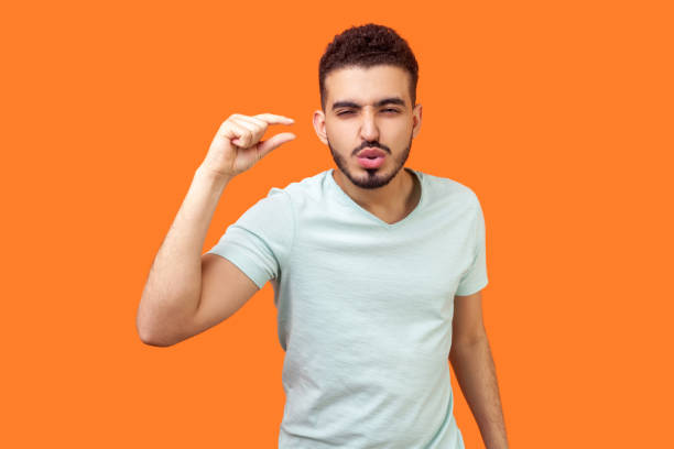 Need some more. Portrait of displeased brunette man showing a little bit or small size gesture. isolated on orange background Need some more. Portrait of displeased brunette man with beard in white t-shirt standing showing a little bit or small size gesture with fingers. indoor studio shot isolated on orange background pleading photos stock pictures, royalty-free photos & images