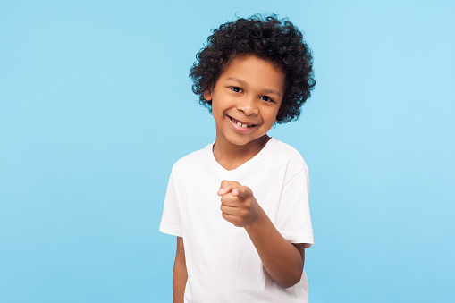 Hey you! Portrait of cheerful funny little boy with curly hair pointing finger to camera and smiling, child making choice indicating at you