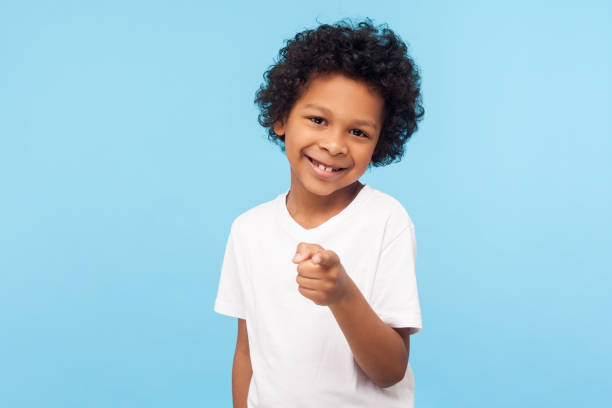 hey you! portrait of cheerful funny little boy with curly hair pointing finger to camera and smiling, child making choice indicating at you - american sign language imagens e fotografias de stock